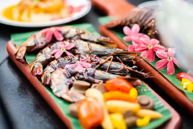 Présentation de crevettes grillées et de légumes colorés sur des feuilles de bananier.