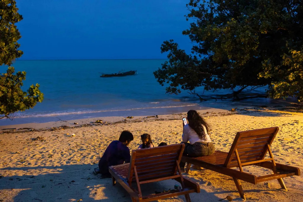 Des personnes sont assises sur une plage de sable au crépuscule.