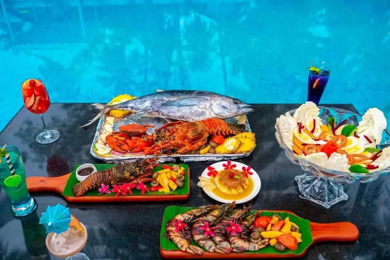 Présentation de fruits de mer et de cocktails sur une table sombre devant une piscine.