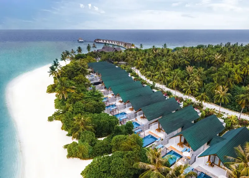 Vue aérienne d'une plage de sable blanc bordée de végétation luxuriante et de bungalows individuels.