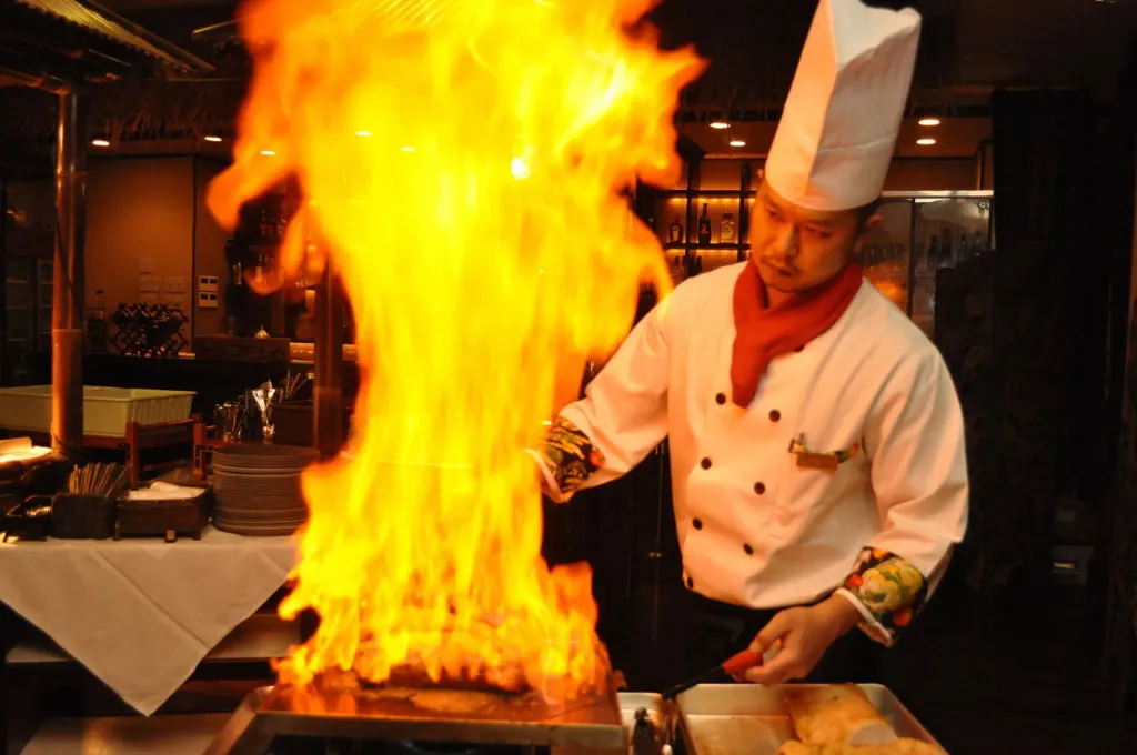 Un chef prépare un plat sur une plaque chauffante avec des flammes.