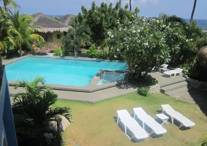Une piscine turquoise bordée d'une pelouse verdoyante et de végétation tropicale.