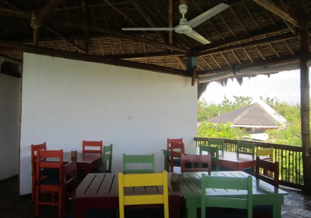 Une salle à manger extérieure avec des tables et des chaises colorées sous un toit de chaume.