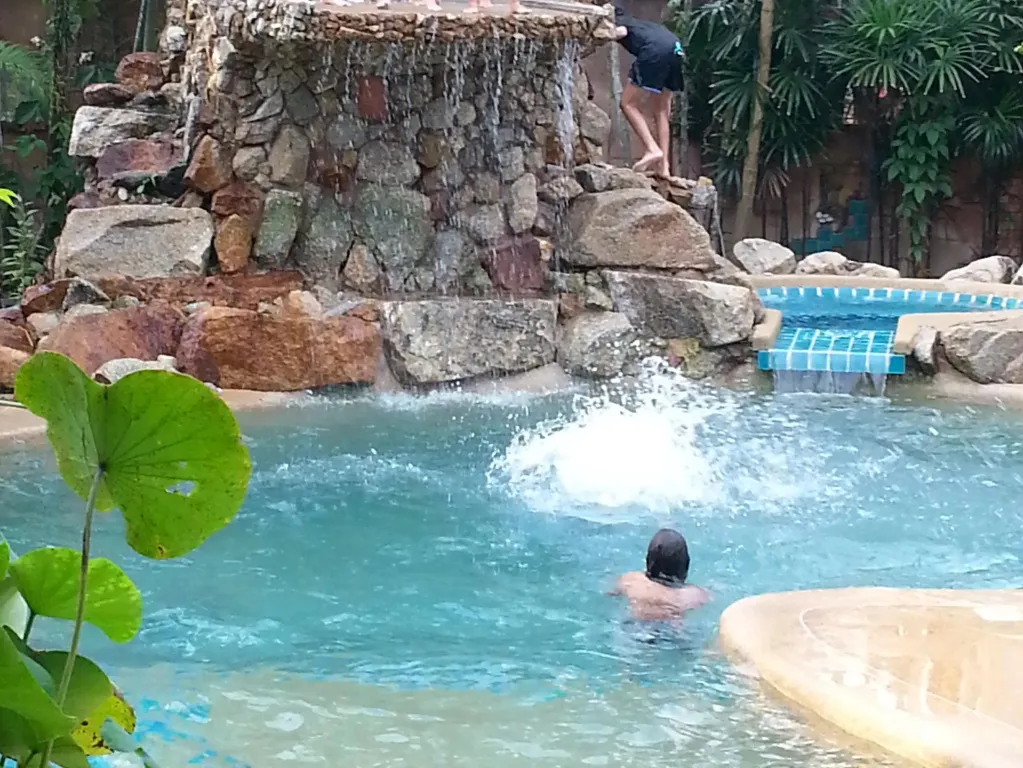 Une personne nage dans une piscine avec une cascade rocheuse en arrière-plan.