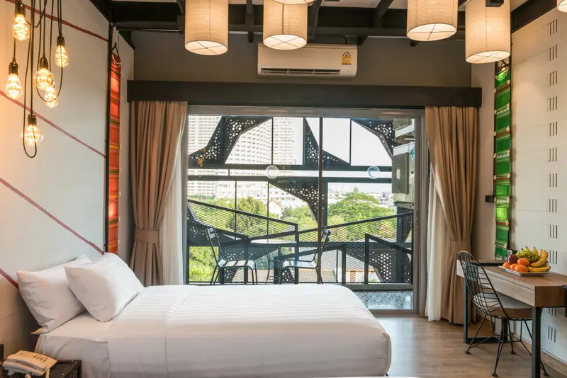 Une chambre lumineuse avec un grand lit et un balcon donnant sur la ville.