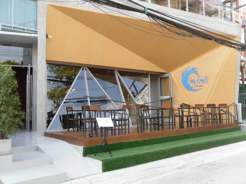 Terrasse ombragée avec tables et chaises devant un bâtiment jaune.
