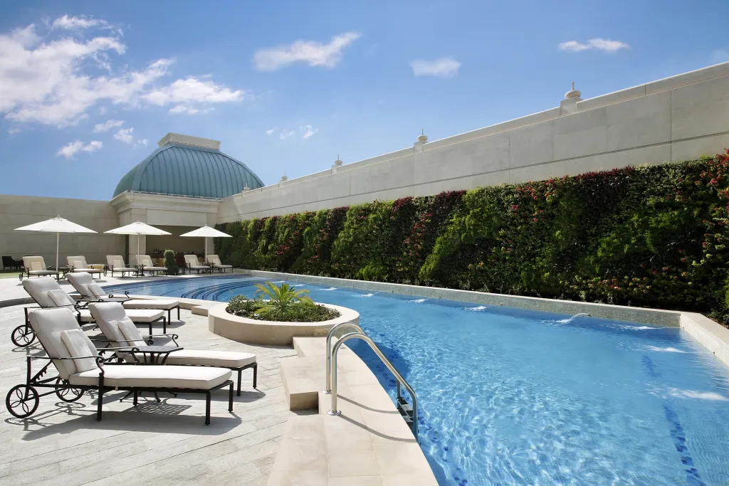 Une piscine rectangulaire avec des transats blancs et un mur végétal.