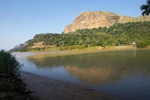 Rivière paisible bordée de végétation luxuriante et de collines rocheuses sous un ciel clair.