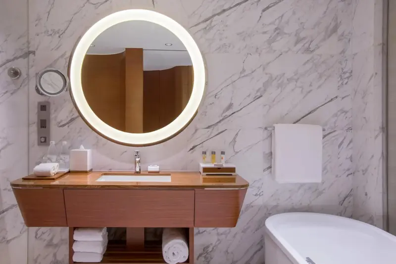 Une salle de bain moderne avec un grand miroir rond et un meuble vasque en bois.
