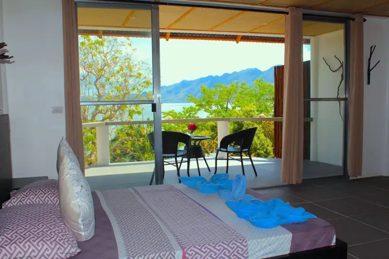 Une chambre avec un lit donnant sur une vue dégagée sur la mer et les montagnes.