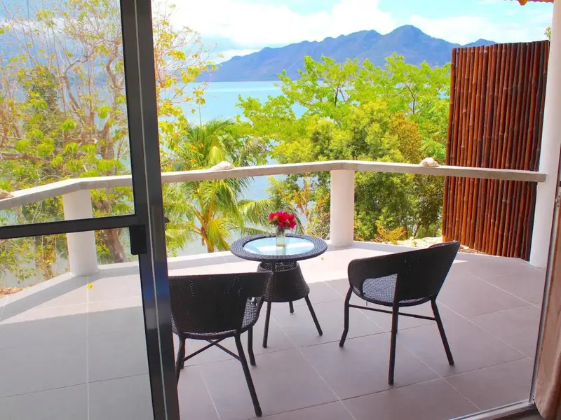 Une terrasse avec une table et des chaises offre une vue sur la mer et les montagnes.