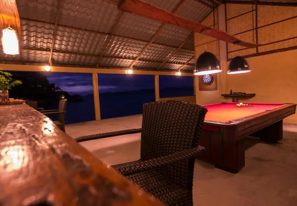 Un espace de détente extérieur avec un bar et un billard offre une vue sur la mer nocturne.