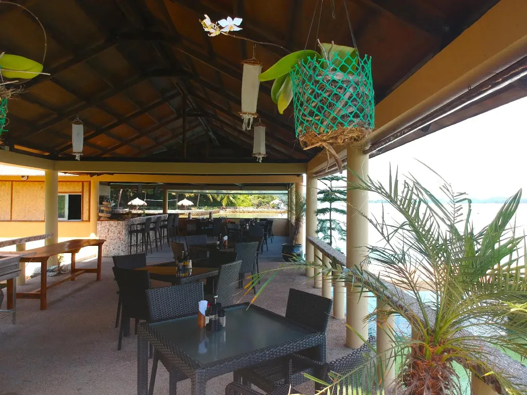 Terrasse ombragée avec tables et bar donnant sur la mer.