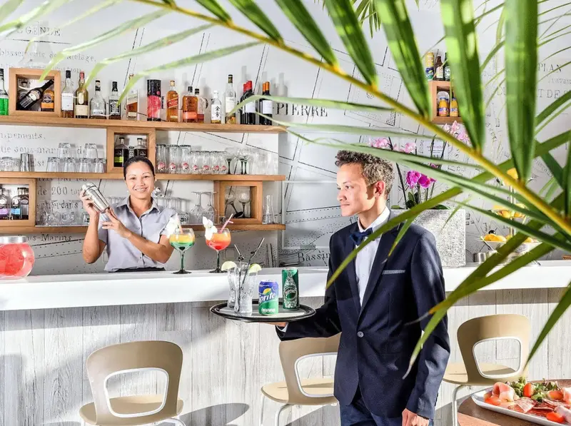 Un barman prépare des cocktails devant un comptoir bien garni.