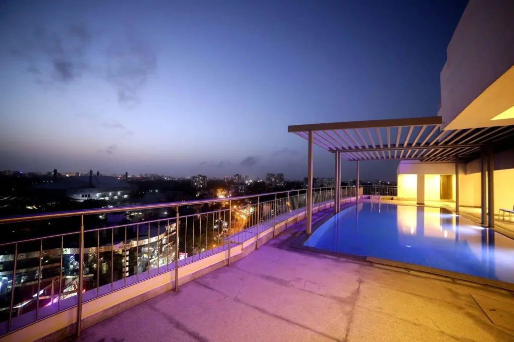 Une piscine illuminée surplombe une ville nocturne.