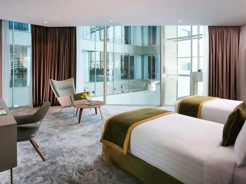 Une chambre lumineuse avec deux lits et un coin salon près d'une grande fenêtre.