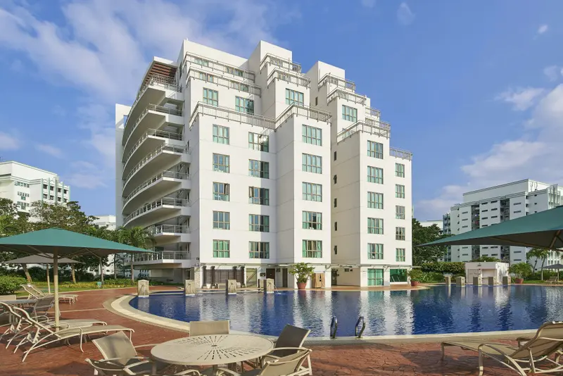 Vue d'un bâtiment blanc avec des balcons surplombant une piscine ensoleillée.