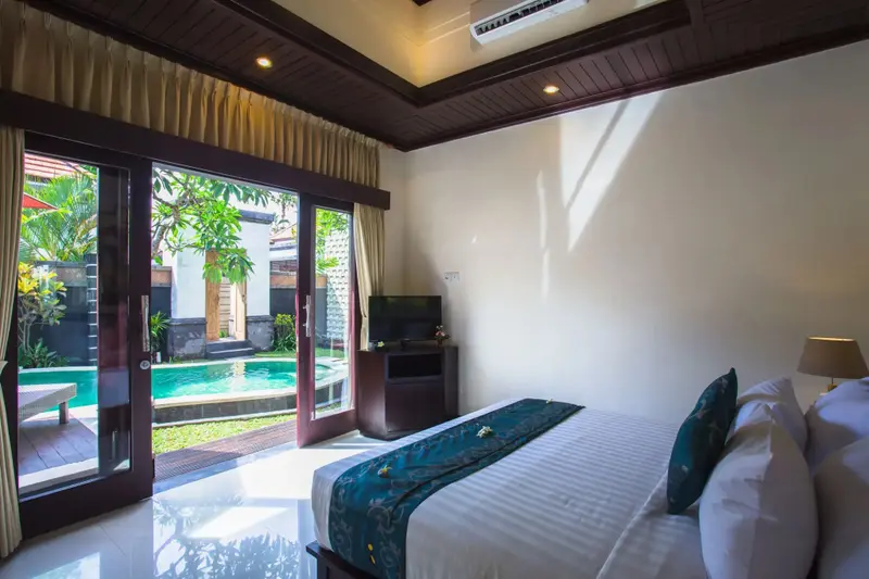 Une chambre lumineuse s'ouvre sur une piscine privée entourée de verdure.