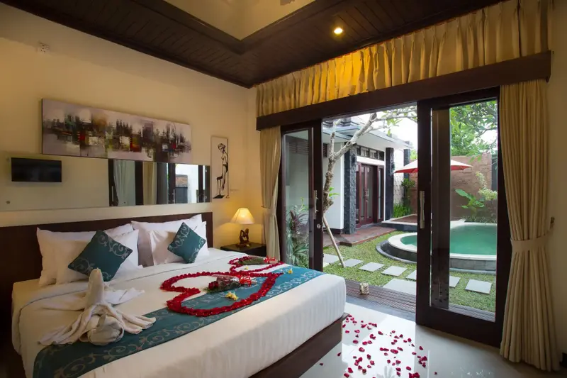 Une chambre lumineuse avec un lit décoré de fleurs et une vue sur une petite piscine extérieure.