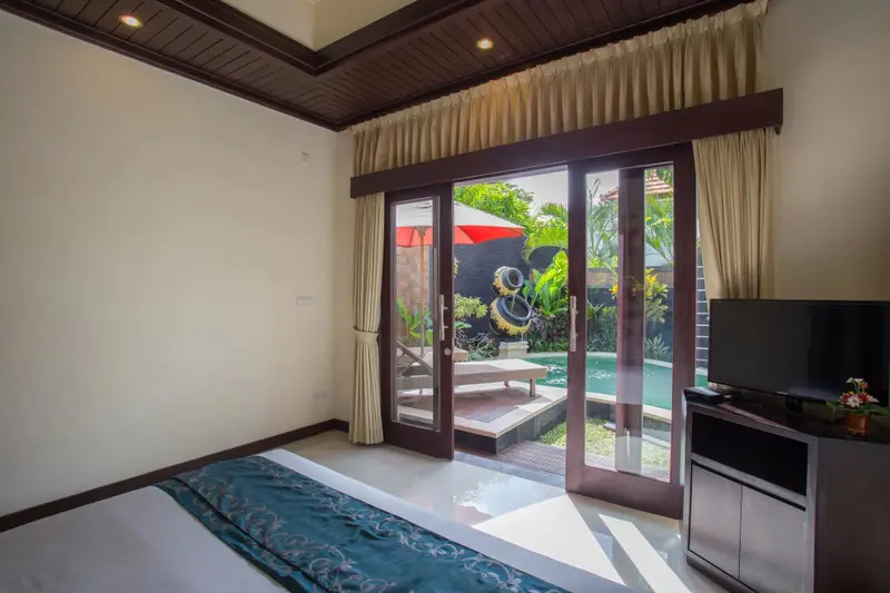Une chambre lumineuse s'ouvre sur une piscine privée entourée de végétation.