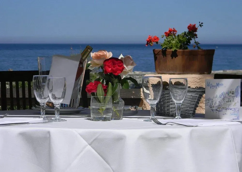 Table dressée avec des verres et des fleurs devant une vue sur la mer.