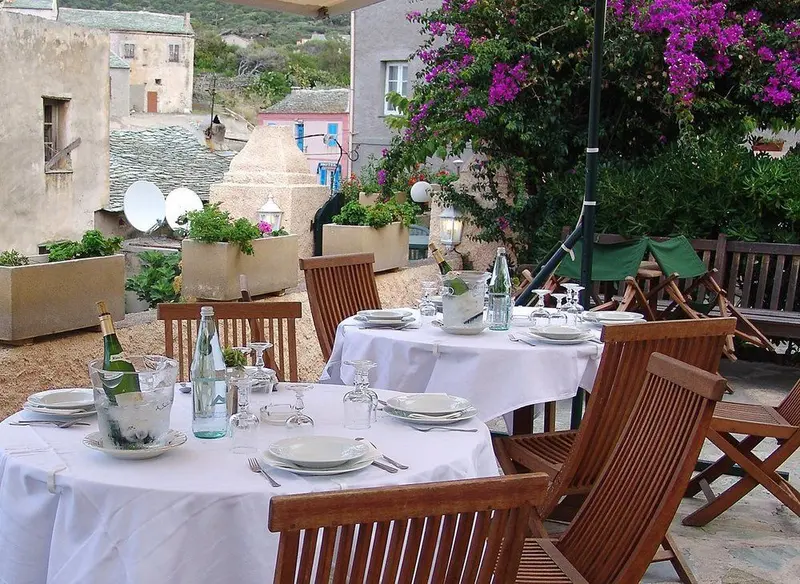 Tables dressées en terrasse avec vue sur des bâtiments et une végétation luxuriante.