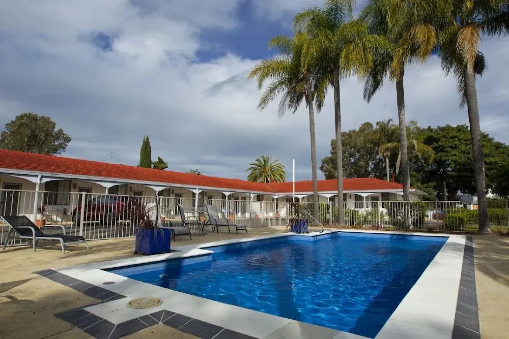 Une piscine rectangulaire entourée de transats et de palmiers sous un ciel nuageux.