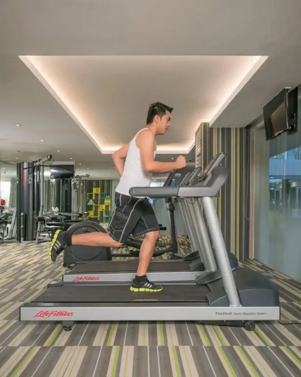 Un homme s'entraîne sur un tapis de course dans une salle de sport lumineuse.