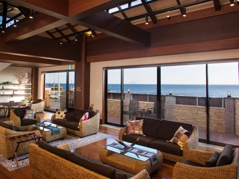 Un espace de détente intérieur avec des canapés et des fauteuils face à une baie vitrée donnant sur la mer.