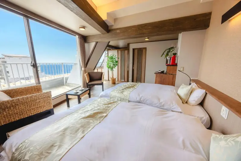 Chambre lumineuse avec deux lits et vue sur la mer par de grandes fenêtres.