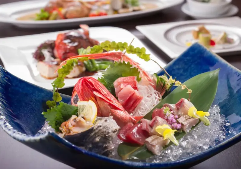Assiette de sashimi de poisson cru, présentée avec des feuilles de salade et des fleurs comestibles.