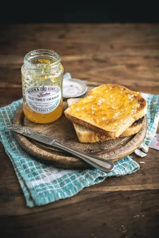 Tartines beurrées et confiture d'orange sur une planche en bois.
