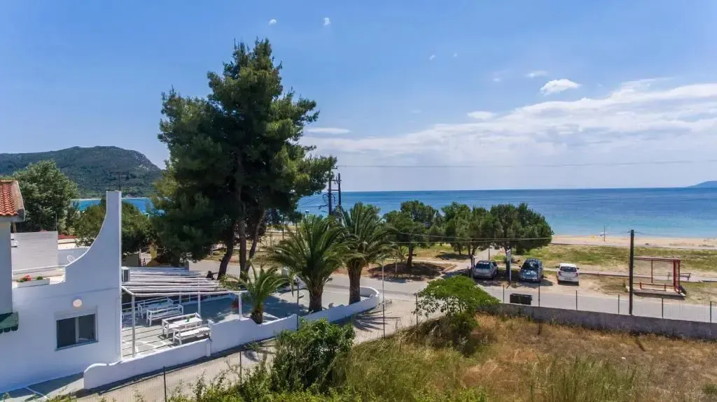 Vue d'un bâtiment blanc avec une pergola donnant sur une plage de sable et la mer.
