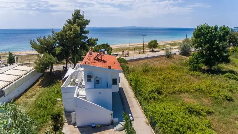 Bâtiment blanc avec toit rouge près d'une plage ensoleillée.