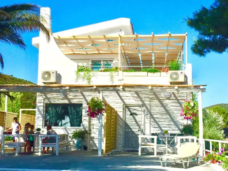 Terrasse ombragée avec mobilier de jardin et bâtiment blanc à l'arrière-plan.