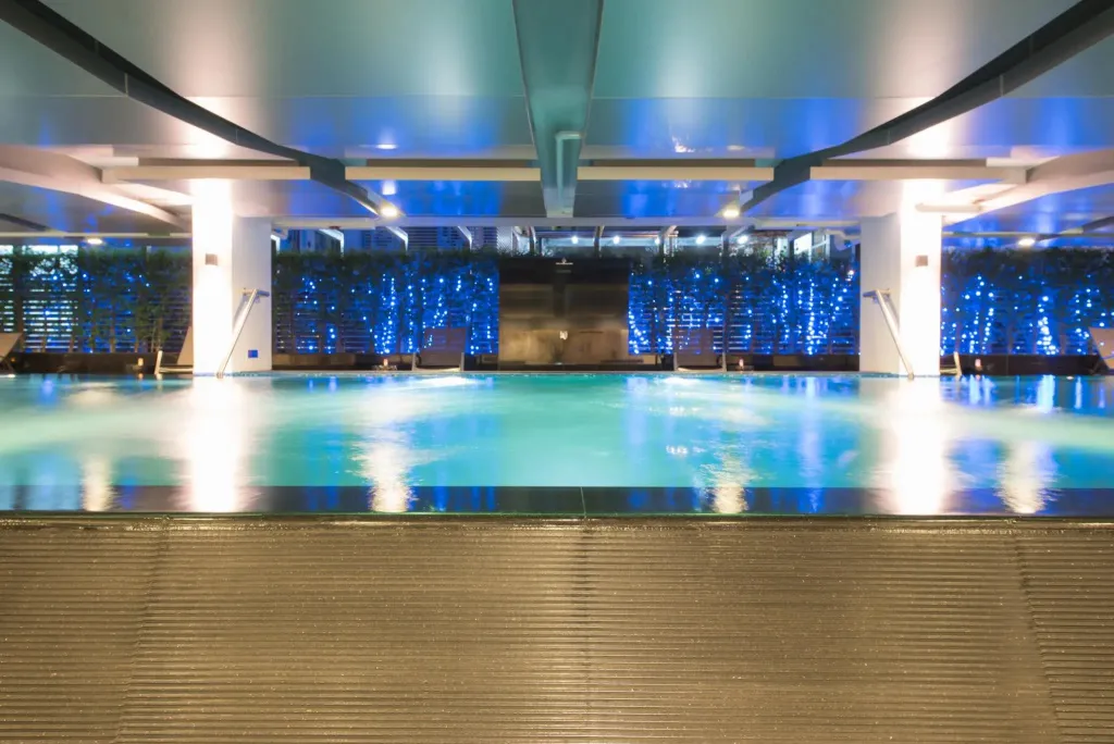 Une piscine intérieure illuminée avec des transats le long du bord.