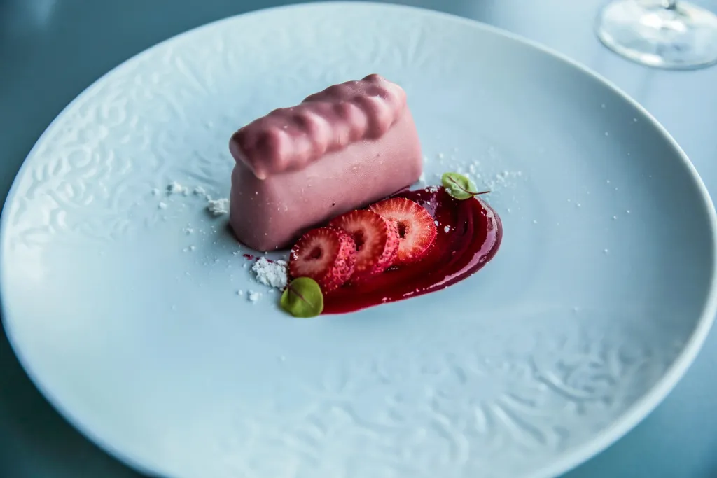 Une assiette présente un dessert à base de fraises et d'une mousse rose.
