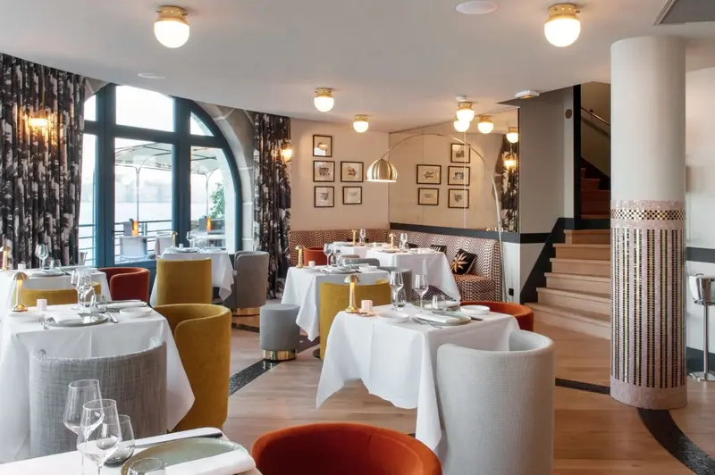 Une salle de restaurant lumineuse avec des tables dressées et des chaises colorées.