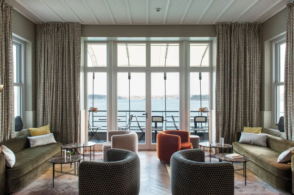 Un espace de détente intérieur avec canapés et fauteuils face à une grande baie vitrée donnant sur la mer.