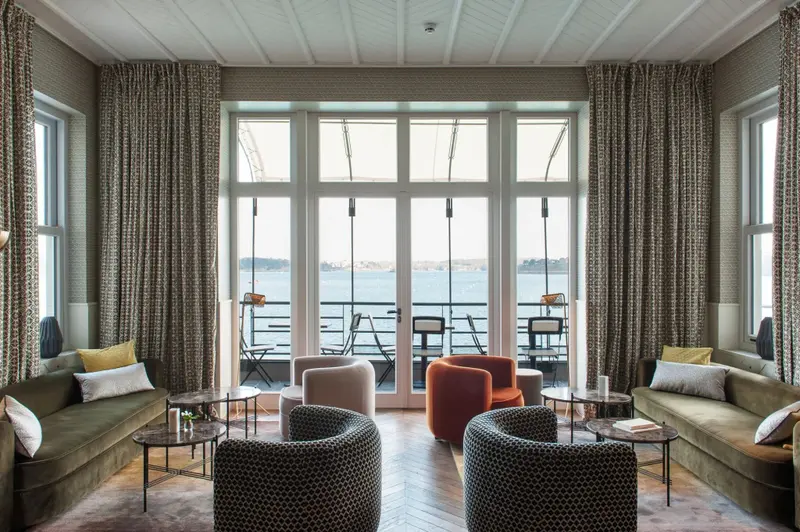 Un espace de détente intérieur avec canapés et fauteuils face à une grande baie vitrée donnant sur la mer.
