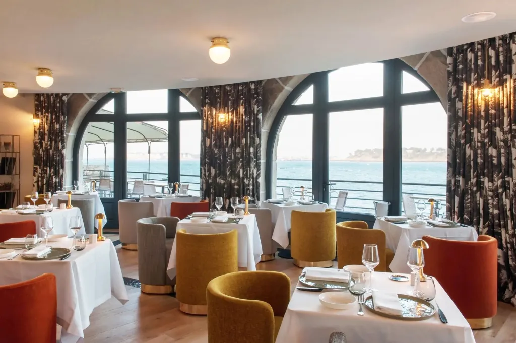 Une salle lumineuse avec des tables dressées face à une vue sur la mer.