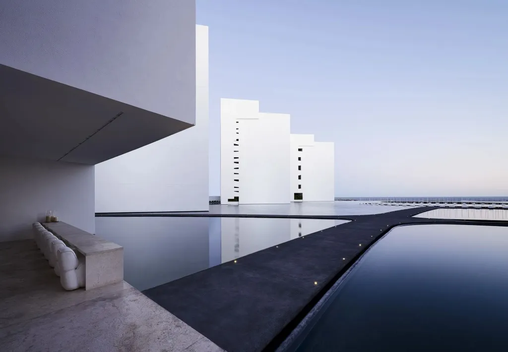 Architecture blanche moderne surplombant une piscine sombre et rectangulaire.