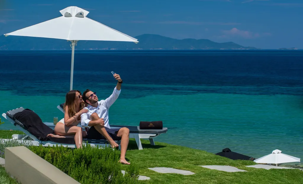 Un couple se prend en photo sur des transats face à la mer turquoise.