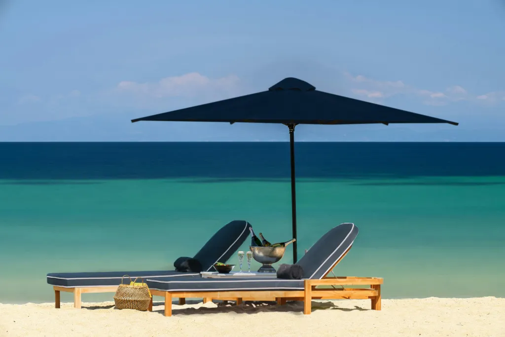 Deux transats ombragés invitent à la détente sur une plage de sable fin face à la mer turquoise.