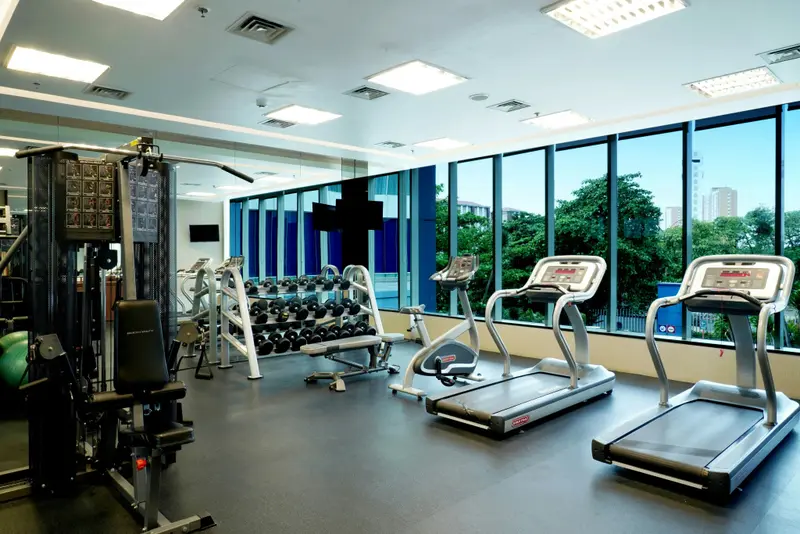 Une salle de sport lumineuse avec des équipements de musculation et des tapis de course face à de grandes fenêtres.