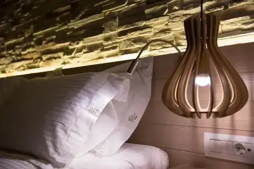 Un lit blanc est éclairé par une lampe de chevet et une suspension en bois.