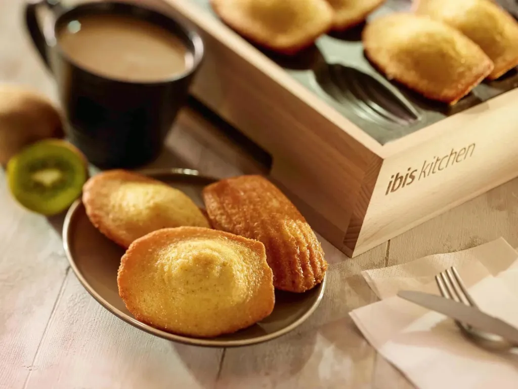 Assiette de madeleines et tasse de café sur une table claire.