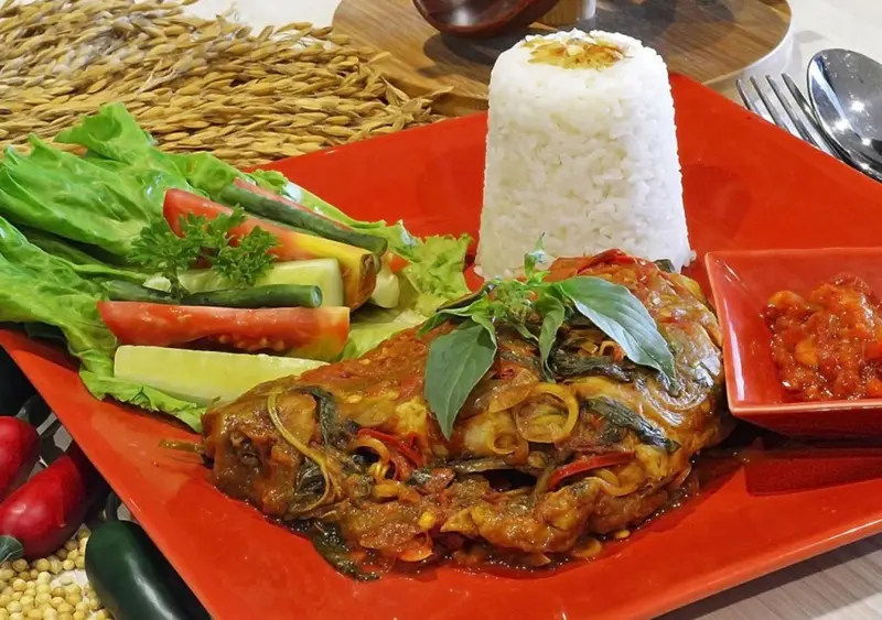 Assiette de poisson épicé accompagné de riz et de légumes frais.