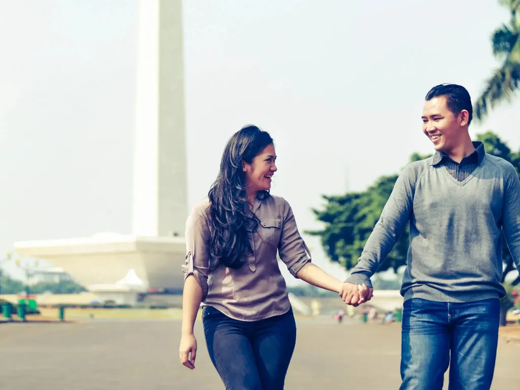 Un couple se promène main dans la main devant un monument.