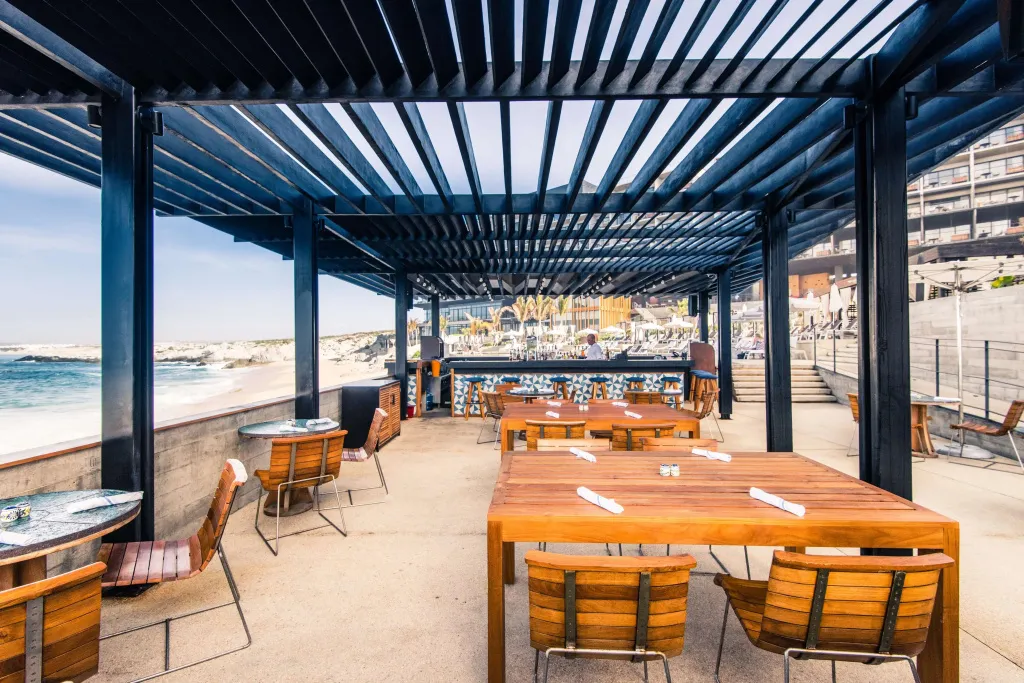 Une terrasse ombragée avec des tables et des chaises en bois donnant sur la mer.